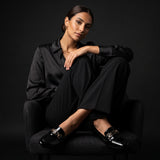 Elegant model in a black suit sitting on a chair wearing classic shiny loafers.