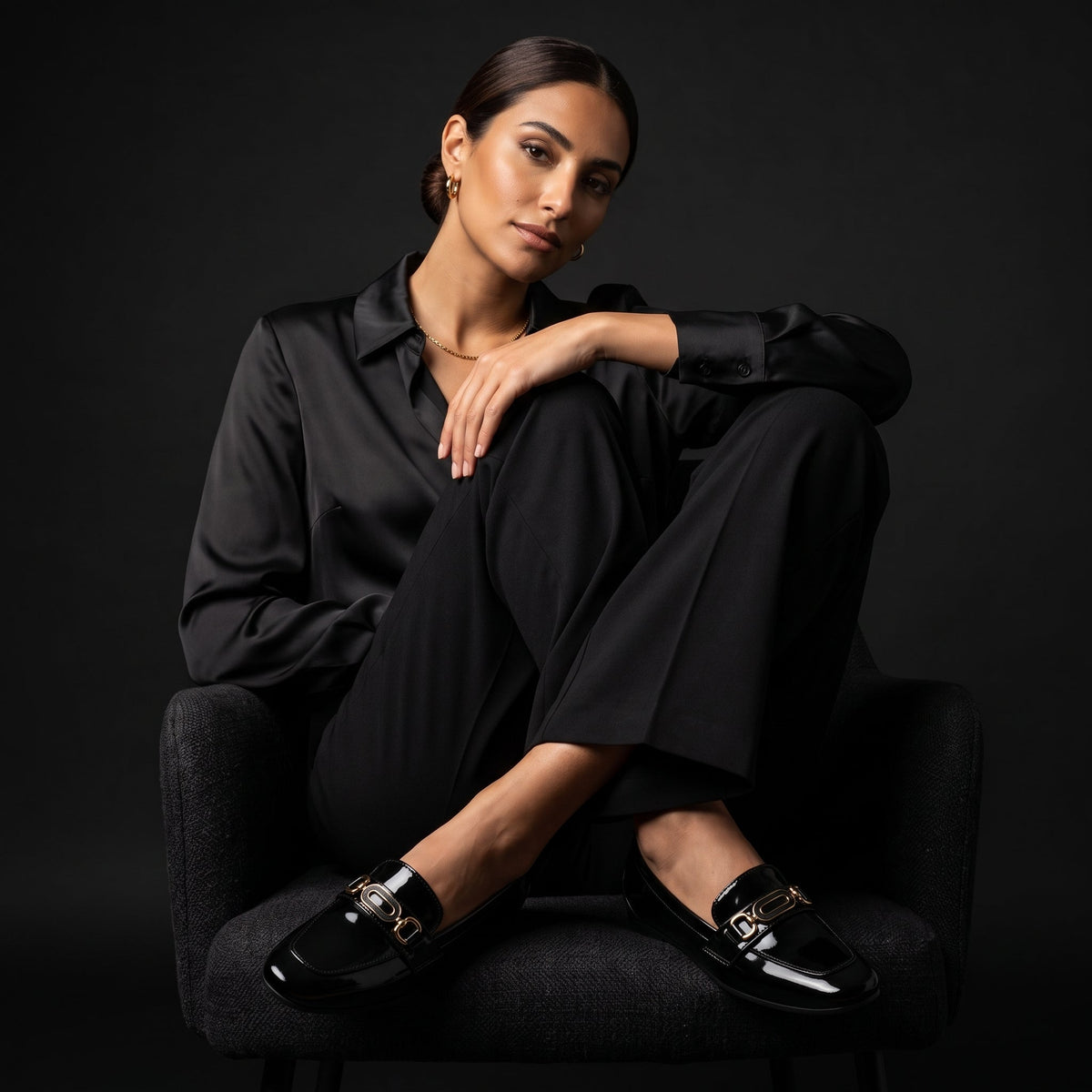 Elegant model in a black suit sitting on a chair wearing classic shiny loafers.