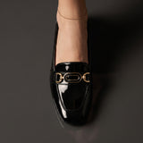 Top down close up of a women's black flat shoe highlighting the gold link buckle.