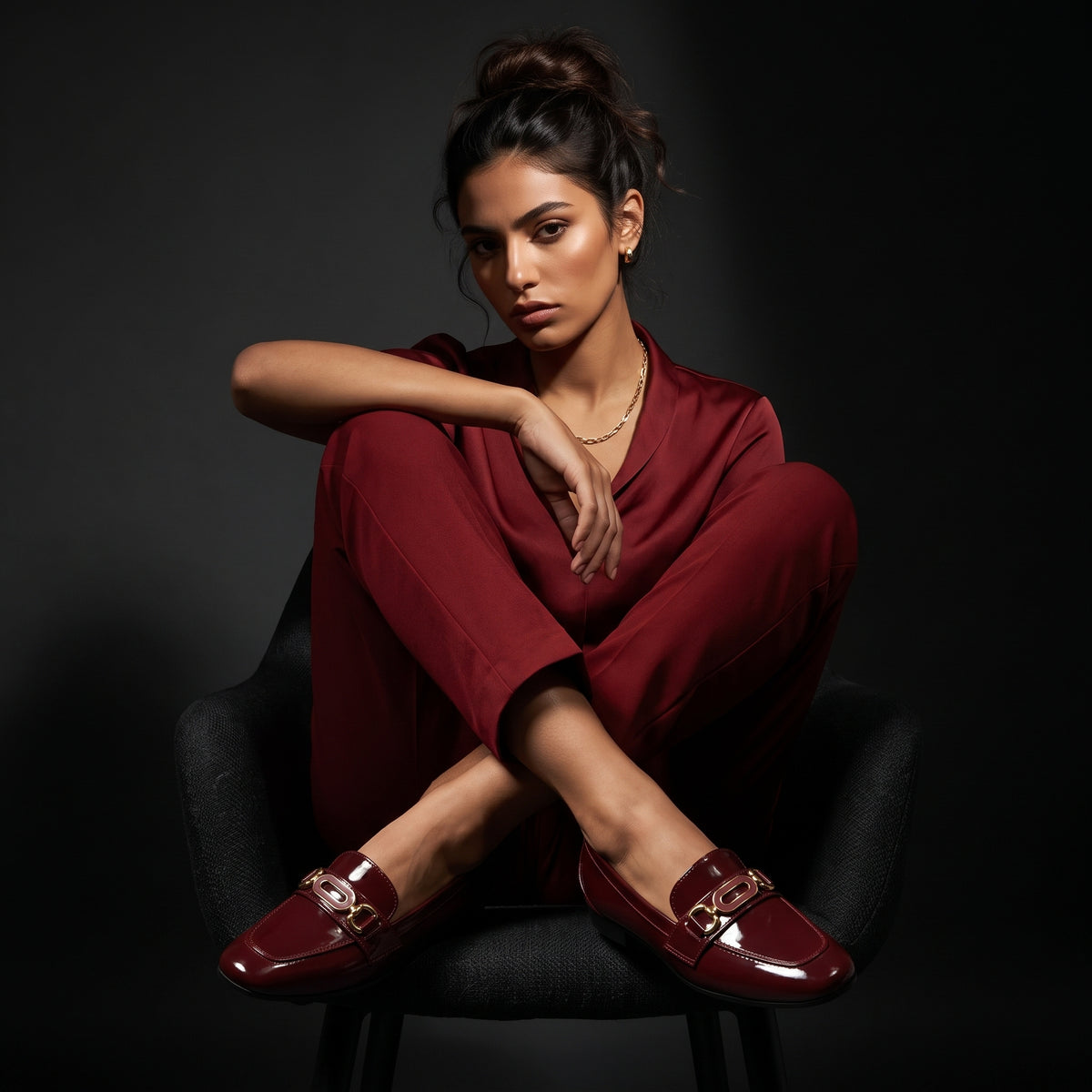 Model sitting gracefully wearing a matching maroon suit and glossy flat shoes in a studio setting.
