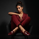 Model sitting gracefully wearing a matching maroon suit and glossy flat shoes in a studio setting.