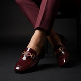 Front view of crossed legs wearing glossy red wine loafers with a classic gold horsebit buckle.
