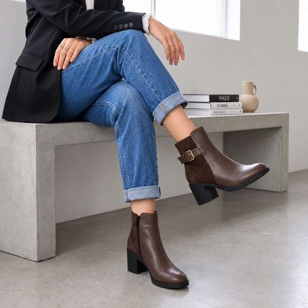 Model sitting on concrete bench wearing dark chocolate brown block heel ankle boots with cuffed jeans and blazer.