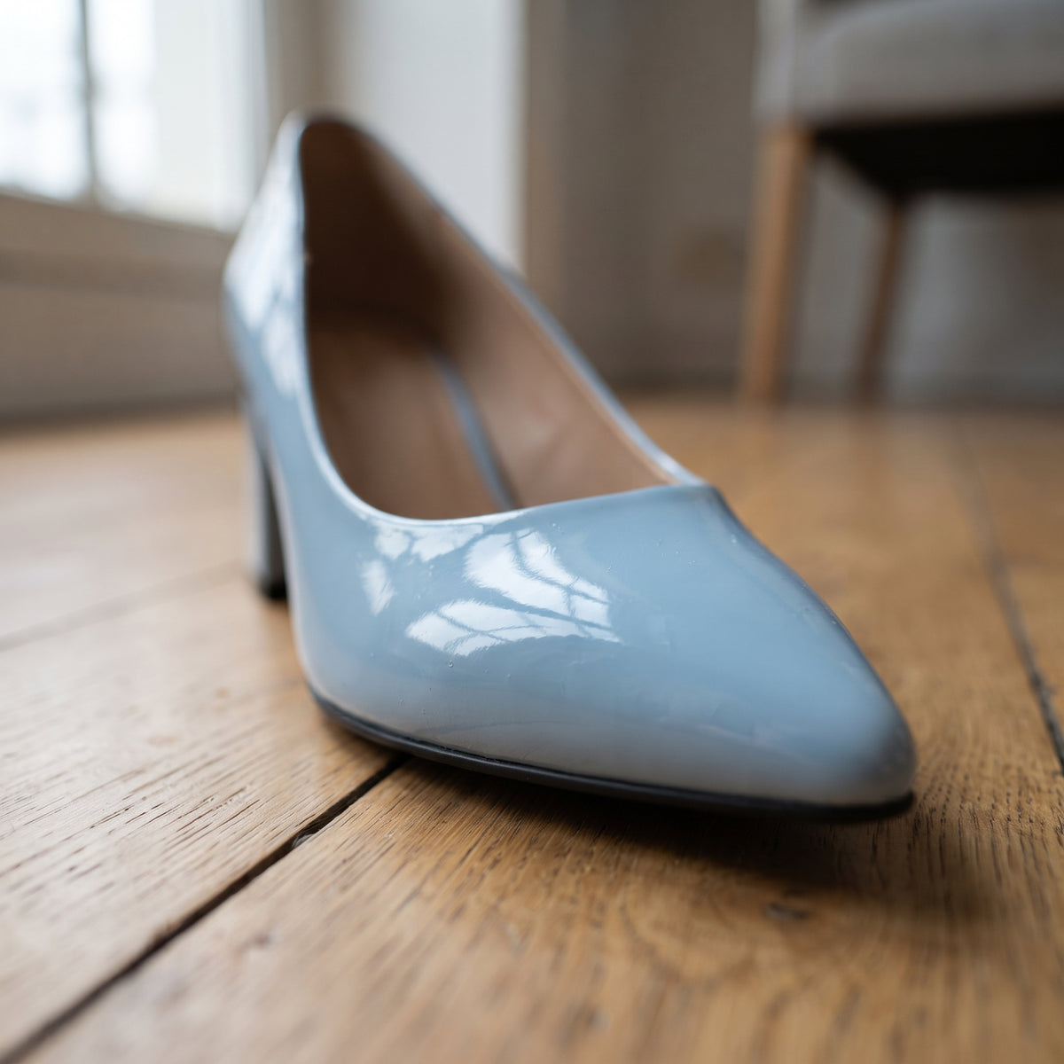 Baby blue patent leather pointed toe pump on wooden floor, low angle close-up showing glossy finish
