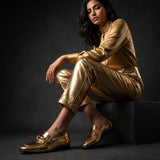 Full lifestyle shot of model sitting on a block wearing metallic gold trousers and shoes.