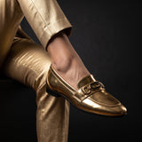 Angle view of metallic gold footwear highlighting the black enamel center buckle.