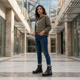 Woman standing in ECADRA Street Mode Nautical Moonlit ankle boots with jeans and olive jacket in modern plaza