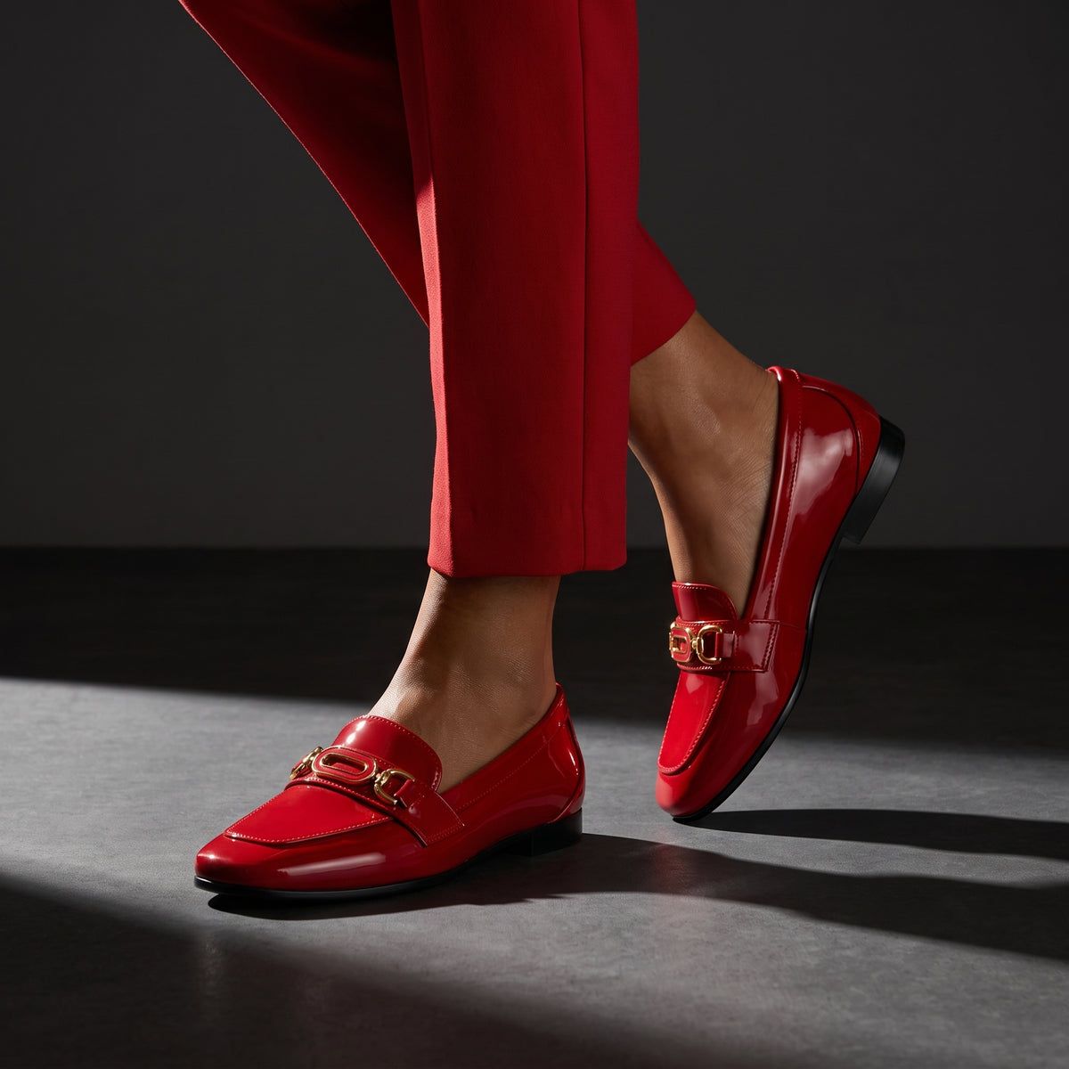 Woman walking in dynamic motion wearing glossy red patent ECADRA loafers with matching red trousers.