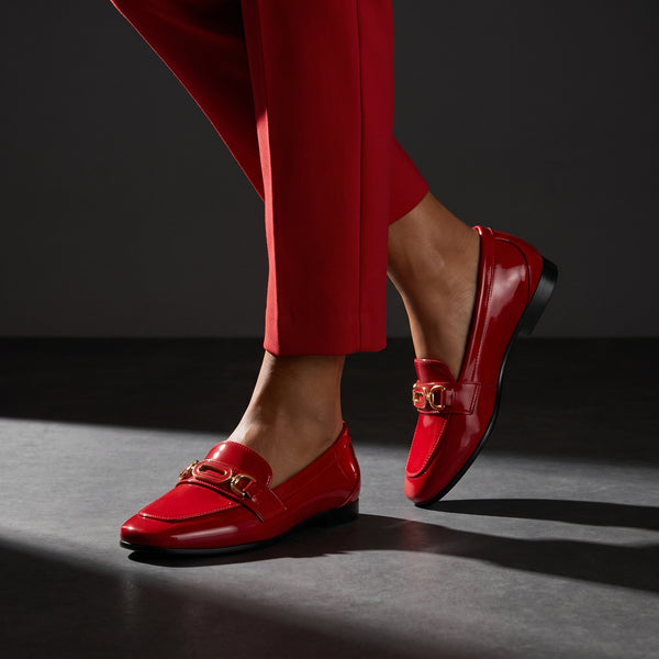 Woman walking in dynamic motion wearing glossy red patent ECADRA loafers with matching red trousers.