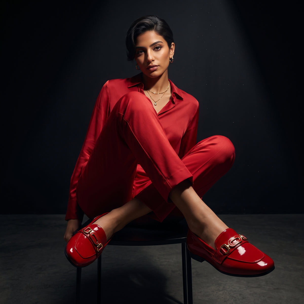 Woman sitting gracefully while wearing glossy red patent ECADRA loafers with gold hardware buckle details and matching red attire.