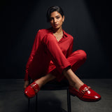 Woman sitting gracefully while wearing glossy red patent ECADRA loafers with gold hardware buckle details and matching red attire.