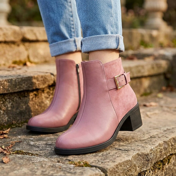 Dusty pink block heel ankle boots with dual leather and suede texture and gold buckle side view on stone steps.