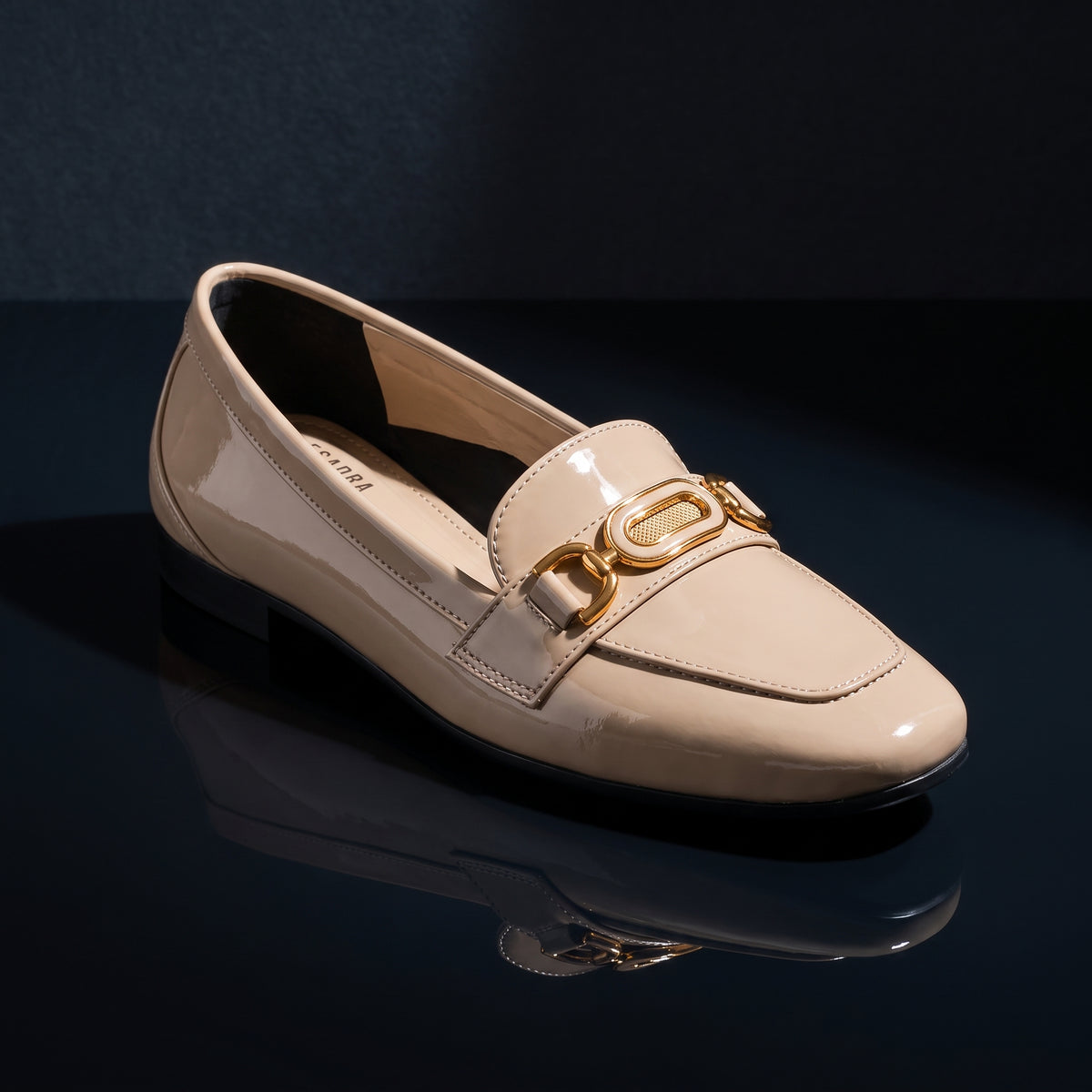 Single glossy beige patent ECADRA loafer displayed on a dark reflective surface, showcasing its gold-tone hardware buckle.