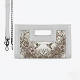 A white rectangular clutch bag with a cutout handle and chain strap, featuring a printed illustration of hummingbirds surrounded by roses and ornate vintage scrollwork 