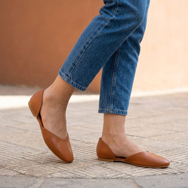 Close-up of tan open-side d'Orsay Wink Flats worn with cropped jeans on stone pavement | ECADRA