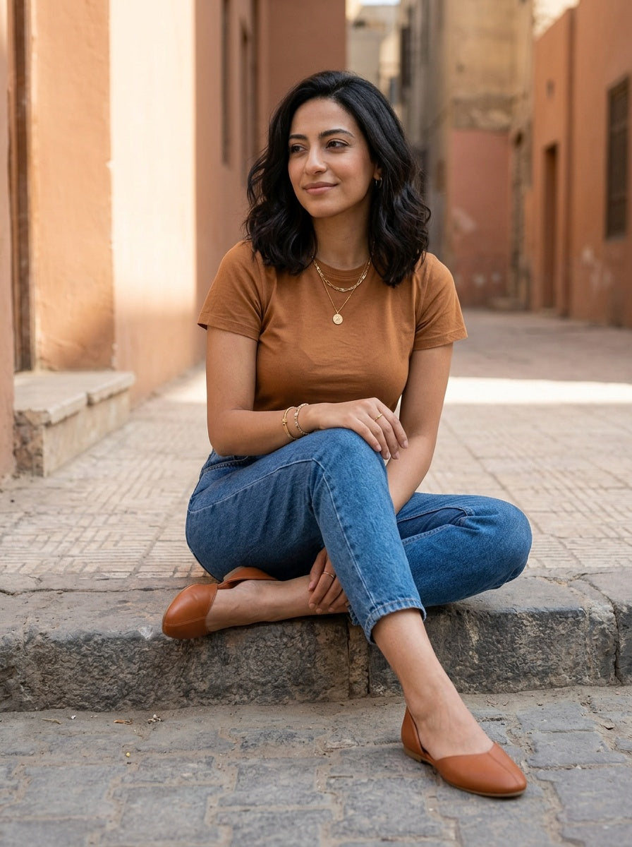 Woman sitting on a step in tan open-side Wink Flats and cropped jeans in soft daylight | ECADRA