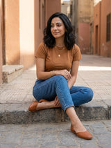 Woman sitting on a step in tan open-side Wink Flats and cropped jeans in soft daylight | ECADRA