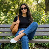 Woman in black top and blue jeans on a park bench wearing white open-side Wink Flats | ECADRA