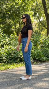 Side view of a woman in white Wink Flats, black top and blue jeans on a sunlit park path | ECADRA