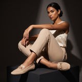 Woman sitting gracefully while wearing glossy beige patent ECADRA loafers with gold hardware buckle details and matching beige attire.