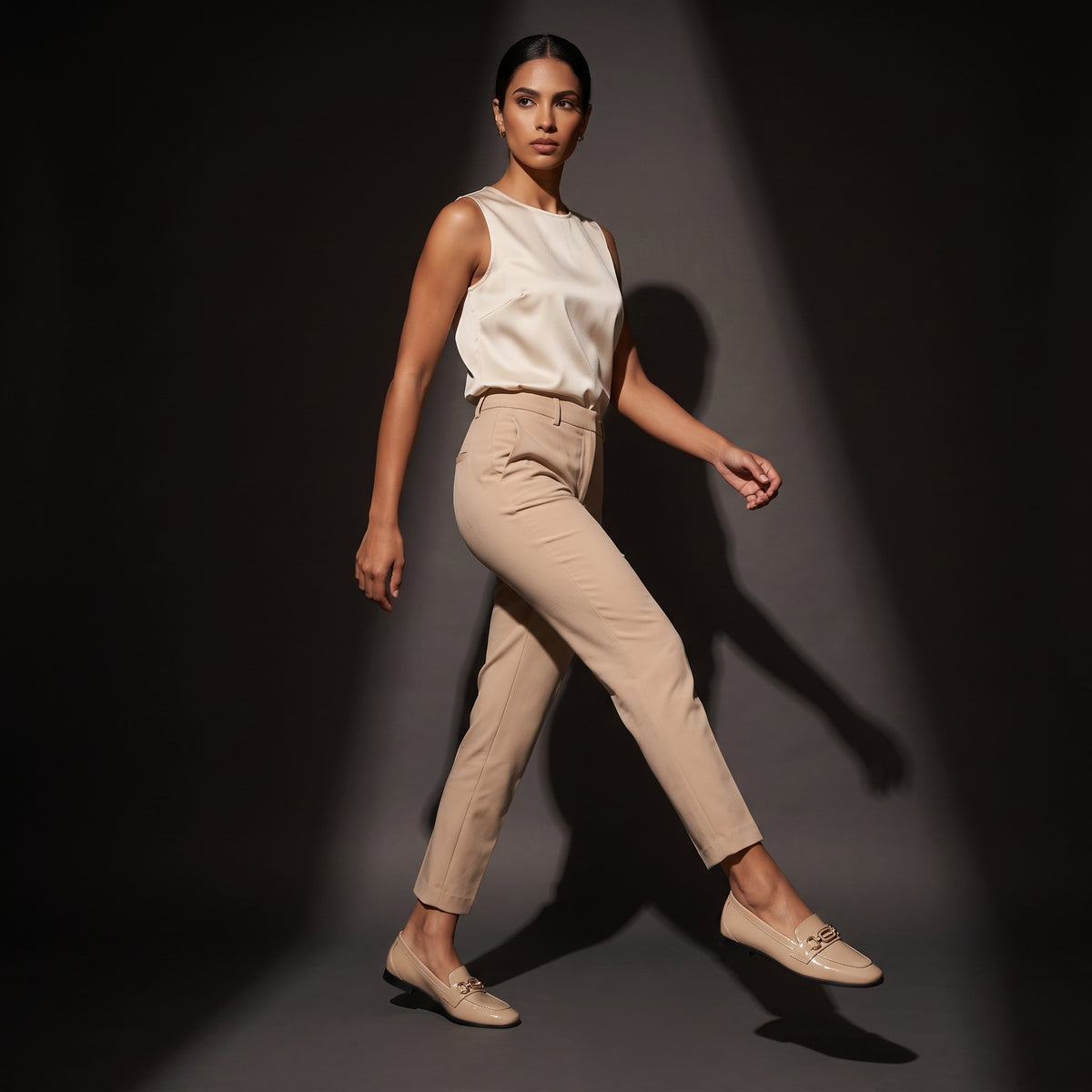 Woman walking forward in dynamic motion wearing glossy beige patent ECADRA loafers with matching beige attire.
