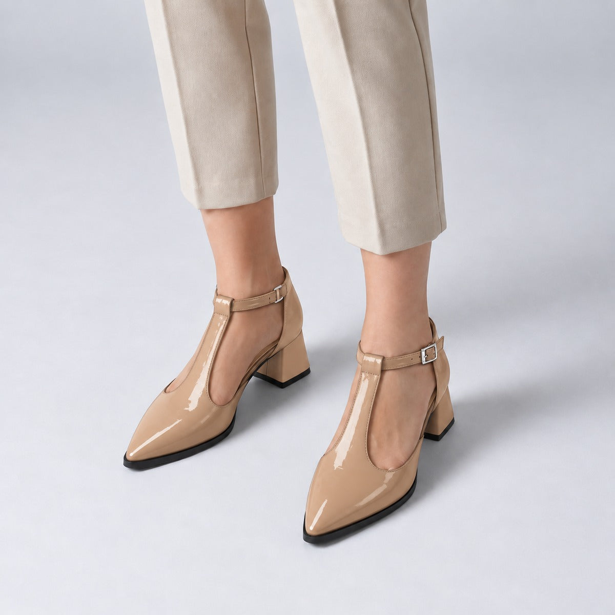 Beige gloss T-strap heels with wide strap, silver buckle and 5 cm flared heel, worn on model, front — ECADRA