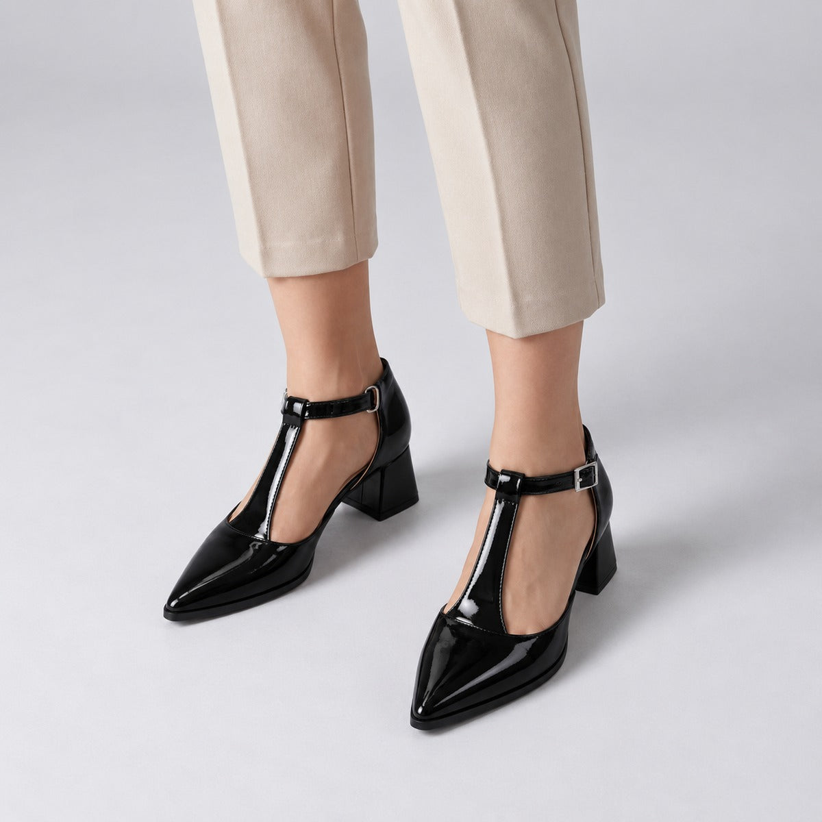 Black gloss T-strap heels with wide strap, silver buckle and 5 cm flared heel, worn on model, front — ECADRA