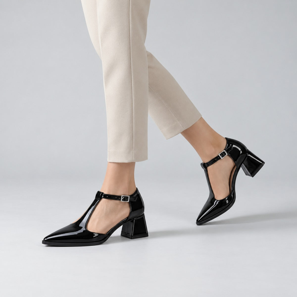 Black gloss T-strap heels with wide strap, silver buckle and 5 cm flared heel, worn on model, walking — ECADRA