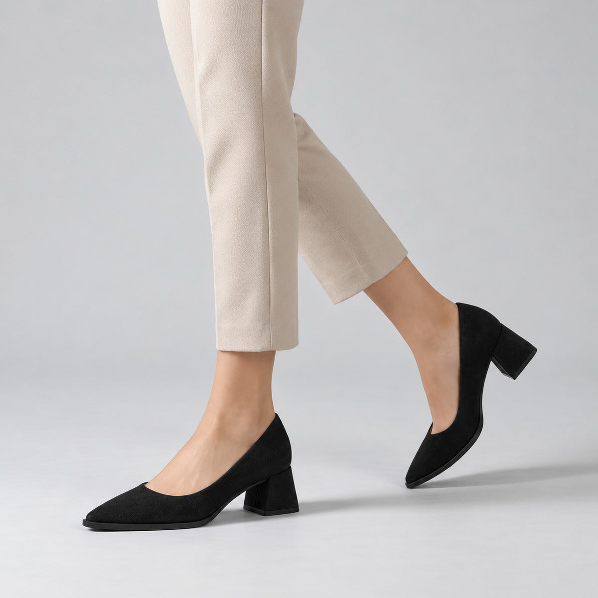 Black suede pointed pump with low 5 cm flared block heel, worn on model, walking — ECADRA