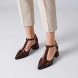 Brown gloss T-strap heels with wide strap, silver buckle and 5 cm flared heel, worn on model, front — ECADRA