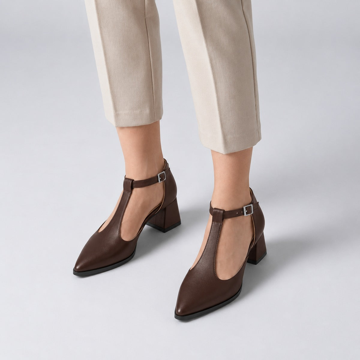 Brown matte T-strap heels with wide strap, silver buckle and 5 cm flared heel, worn on model, front — ECADRA