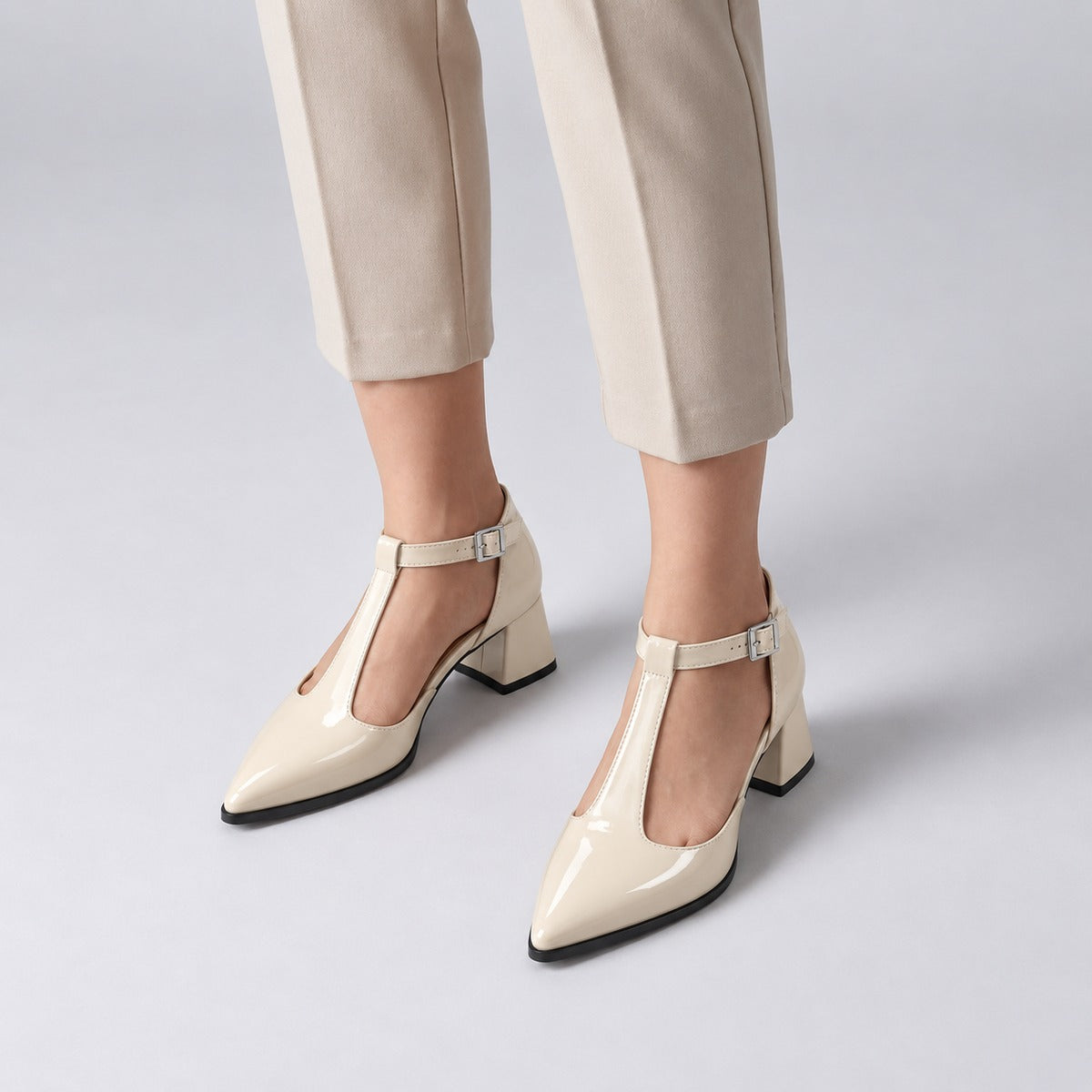 Cream gloss T-strap heels with wide strap, silver buckle and 5 cm flared heel, worn on model, front — ECADRA