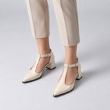 Cream gloss T-strap heels with wide strap, silver buckle and 5 cm flared heel, worn on model, front — ECADRA