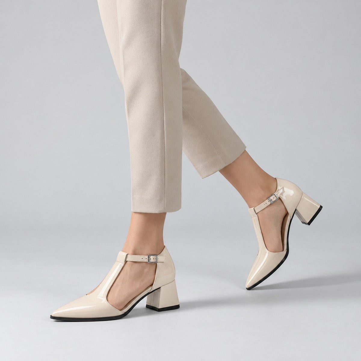Cream gloss T-strap heels with wide strap, silver buckle and 5 cm flared heel, worn on model, walking — ECADRA