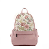 A structured mini backpack with a pink faux leather base and a top flap made of woven fabric printed with a vintage pattern of pink, mauve, and purple flowers with green leaves and gold filigree accents, featuring a front zipper and side pockets.
