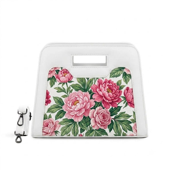 A vibrant arrangement of vintage pink peonies, roses, and green leaves is featured on the front panel of a structured white top-handle handbag with a detachable shoulder strap.
