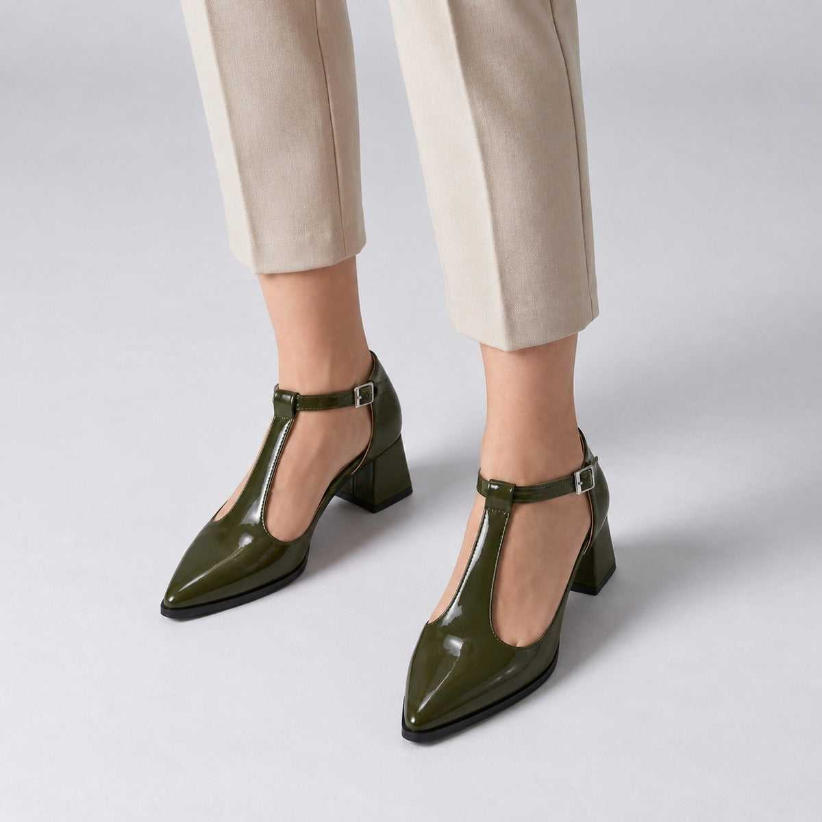 Olive gloss T-strap heels with wide strap, silver buckle and 5 cm flared heel, worn on model, front — ECADRA