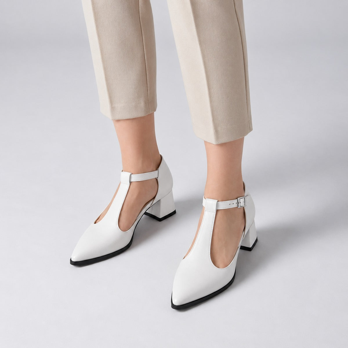 White matte T-strap heels with wide strap, silver buckle and 5 cm flared heel, worn on model, front — ECADRA